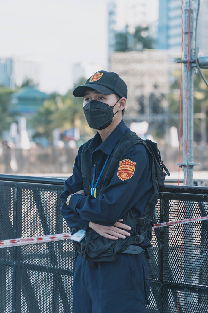 Security guard wearing a mask and uniform standing outdoors ensuring safety.