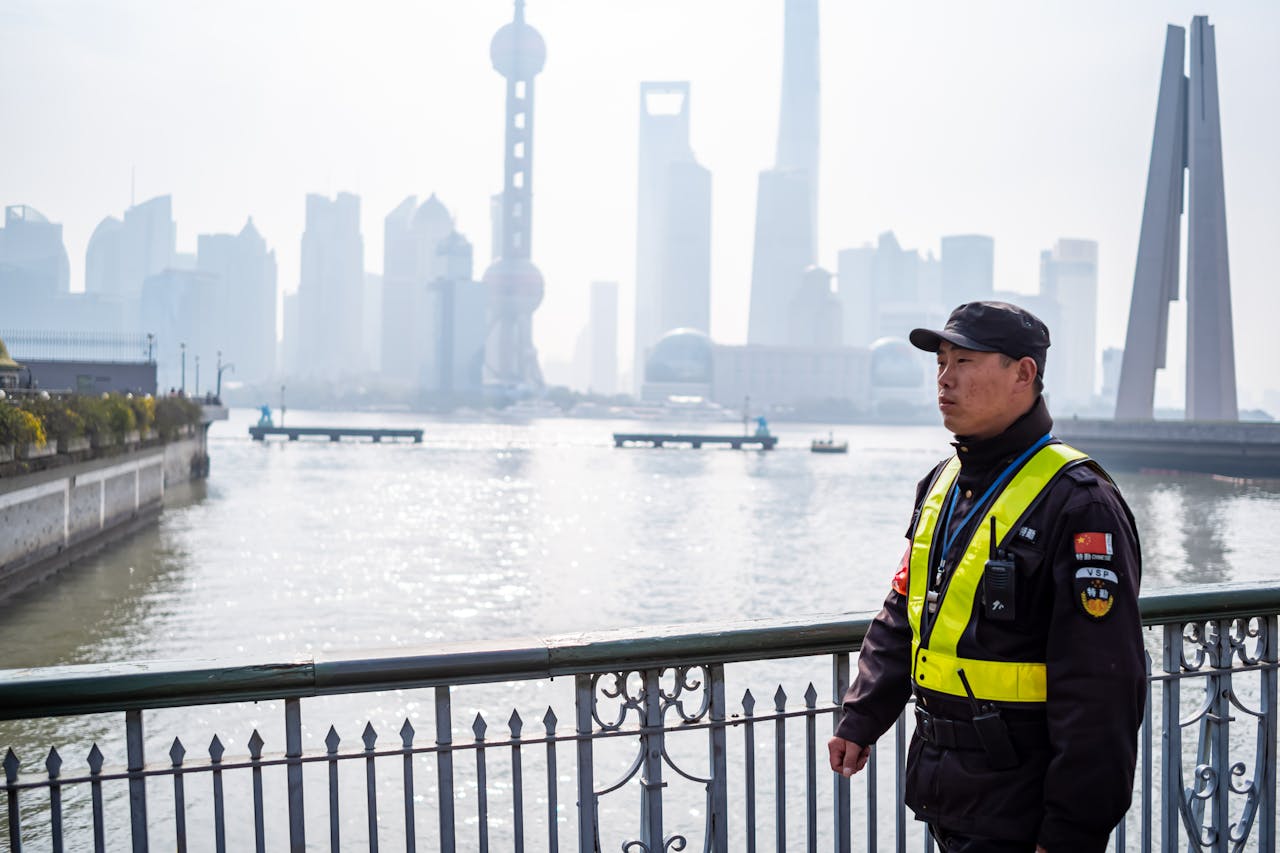 A police officer in uniform on a bridge with Shanghai urban skyline and river background.